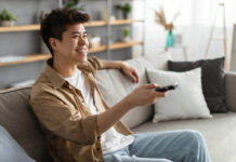 Transformers: Rise of the Beasts Smiling man sitting on the couch using the TV remote to search for new movies to watch