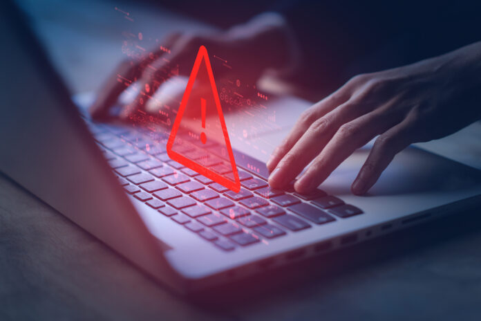 System hacked warning alert on notebook (Laptop). Cyber attack on computer network, Virus, Spyware, Malware or Malicious software. Cyber security and cybercrime. Compromised information internet. Hands typing on a laptop with an icon of a warning label depicting illegal activities.