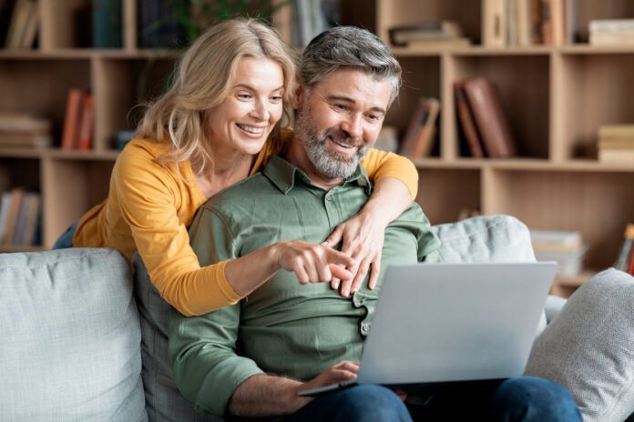 Happy Middle Aged Couple With Laptop Ordering Things From Internet Together Middle aged couple smiling while safely browsing the Internet on a laptop
