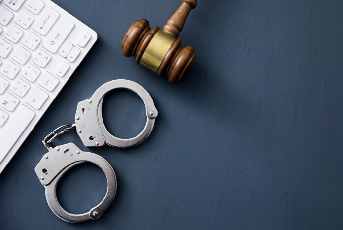 WhatHappensIf_shutterstock_2316965491 A computer keyboard with handcuffs and a judge’s gavel.